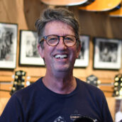 man wearing glasses guitars in background